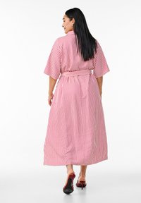 Vestido maxi a rayas en rojo y rosa, ceñido en la cintura, con mangas cortas y tejido fluido que llega por debajo de los tobillos.