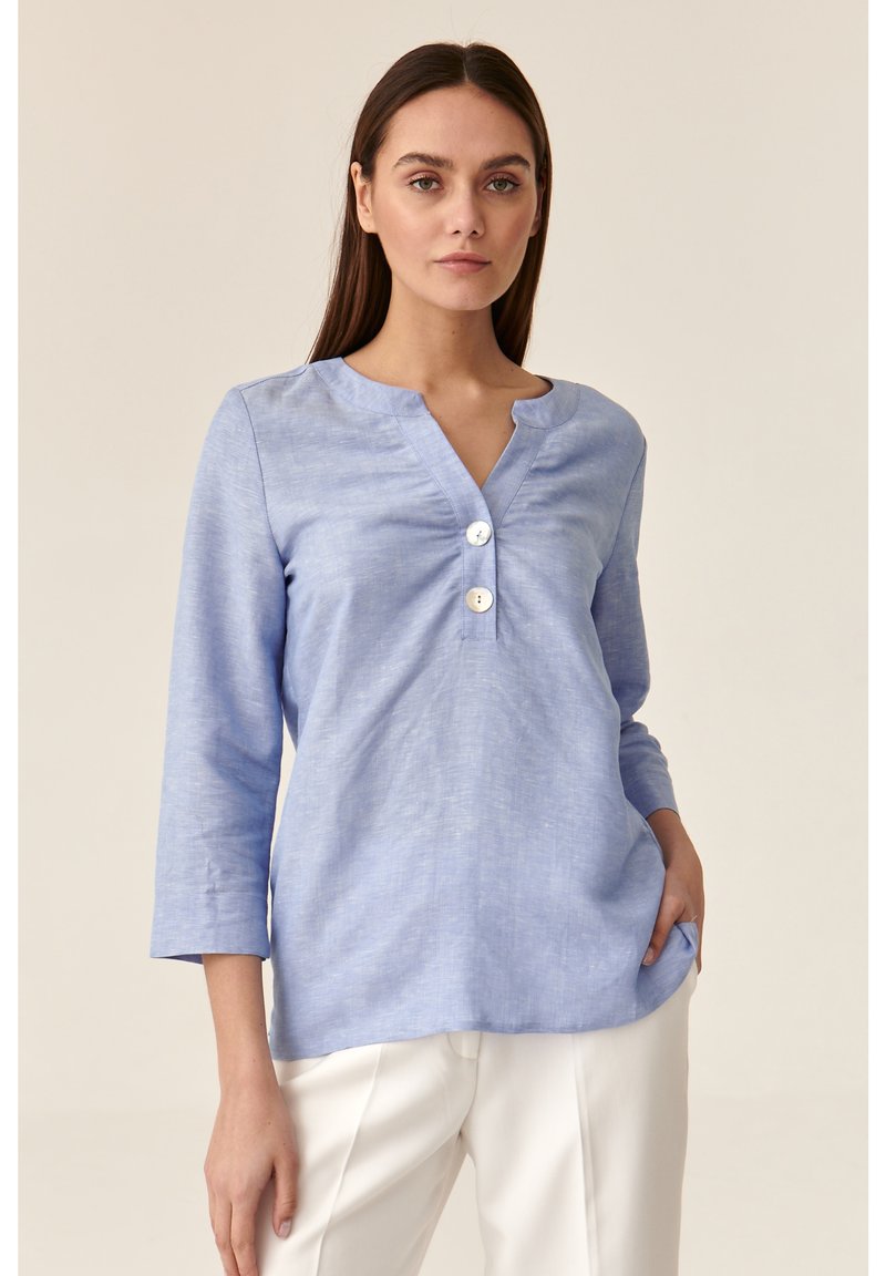 Blusa azzurra chiara a maniche lunghe con scollatura a V, tre bottoni sul davanti e una vestibilità morbida. Il tessuto ha una leggera texture.
