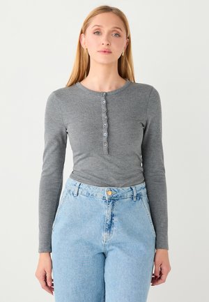Haut gris à manches longues avec encolure ronde et patte de boutonnage à six boutons, associé à un jean en denim bleu clair taille haute montrant des poches avant.