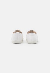 Les baskets en toile blanche présentent une forme arrondie, une tige texturée et une semelle en caoutchouc rayée contrastante. Le talon est doux et rembourré.