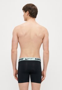 Mustad Nike bokserid helel sinise vöökohaga, millel on brändinimi mustas kirjas. Vaade tagant, sile kangas ja keha järgnev lõige.