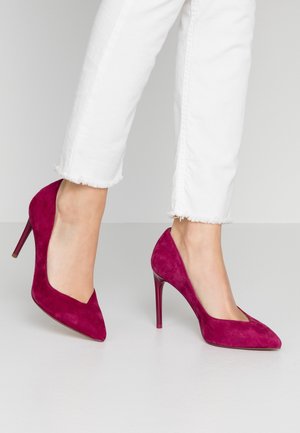 Fuchsia suède hoge hakken met een spitse neus, slanke stiletto hak en een strak ontwerp, gecombineerd met witte jeans met rafels aan de onderkant.