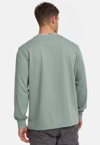 Langærmet sweatshirt med rund hals i blød, afdæmpet grøn bomuldsblanding. Har ribbede manchetter og et subtilt logo detaljeret ved halsudskæringen.