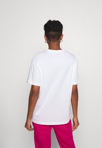 T-shirt bianco a maniche corte con vestibilità rilassata. Il tessuto sembra morbido. Caratteristiche notevoli includono un colletto tondo e un design semplice.