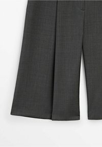 Un pantalon gris ajusté en tissu texturé, avec une coupe large et des plis sur le devant. L'ourlet est droit, sans embellissements supplémentaires.