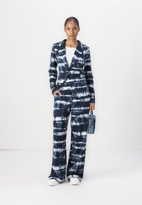Marineblauw en witte tie-dye pak, met een blazer met een notch lapel en brede broekspijpen. Gecombineerd met een kleine blauwe handtas.