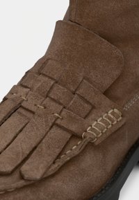 Botte en daim marron avec des détails tissés, surface texturée, accents cousus et semelle noire. Gros plan sur les caractéristiques de conception et les matériaux.