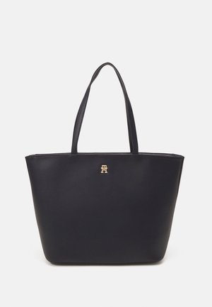 Black leather tote bag with two shoulder straps, featuring a gold logo accent on the front and a spacious, minimalist design.