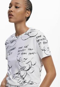 Tricou alb cu mânecă scurtă, prezentând schițe de desene animate negre și text, guler rotund și o croială lejeră. Designul include ilustrații jucăușe ale personajelor.