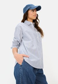Gestreiftes Hemd aus blauem und weißem Baumwollstoff, mit einem Knopfkragen und Brusttasche, kombiniert mit einer blauen Jeanskappe. Legere, lockere Passform.