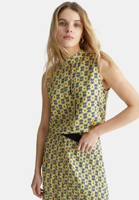 Abito senza maniche con scollatura alta, caratterizzato da un motivo geometrico giallo e blu navy. Tessuto leggero con una consistenza liscia. Dettaglio con cintura nera.