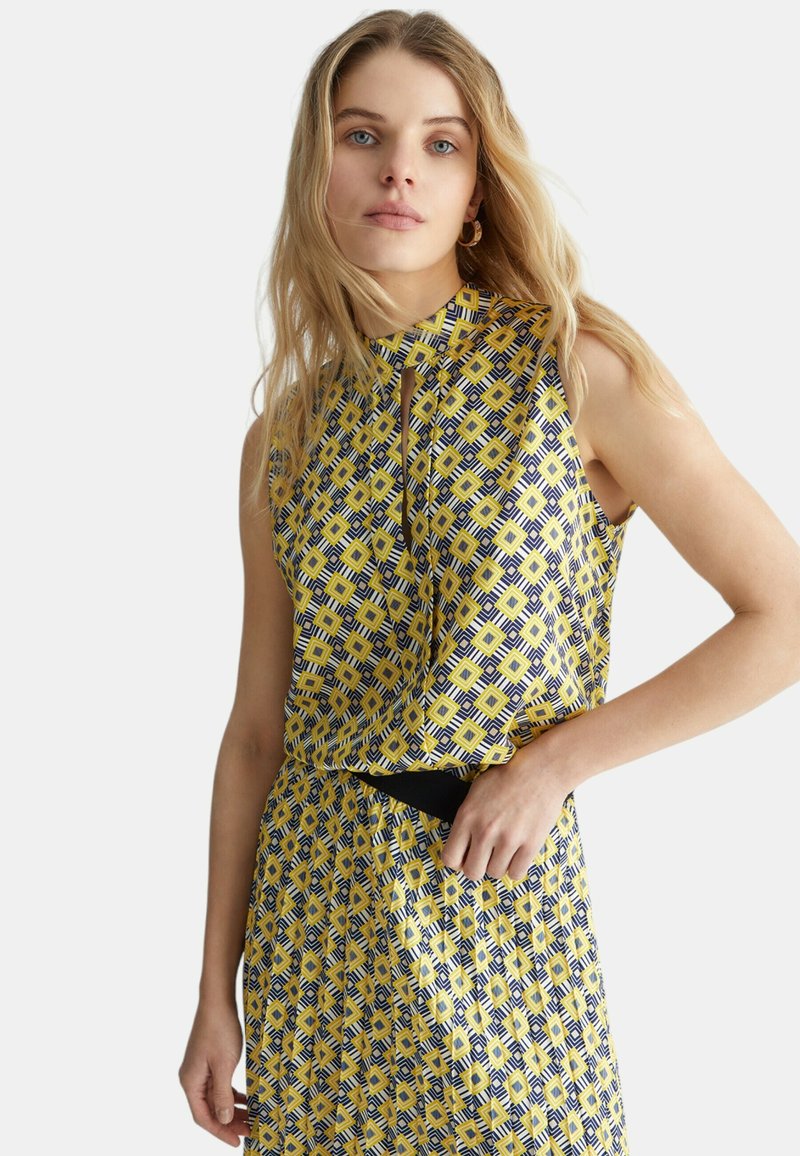Abito senza maniche con scollatura alta, caratterizzato da un motivo geometrico giallo e blu navy. Tessuto leggero con una consistenza liscia. Dettaglio con cintura nera.