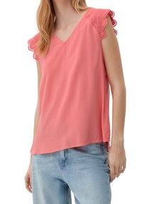 Débardeur corail avec un col en V, orné d'une bordure en dentelle sur les épaules, confectionné en tissu léger, associé à un jean en denim bleu clair.