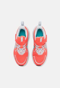 Des chaussures de sport roses vives avec une tige en mesh, des accents blancs et une doublure turquoise. Elles présentent une sangle à velcro et des lacets.