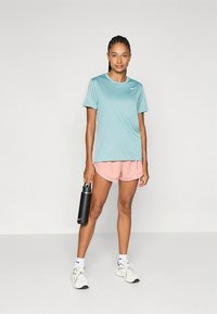 Ljusblå sport-t-shirt, rosa shorts, svart vattenflaska och vita sneakers. Mjukt tyg med Nike-logga på t-shirten.