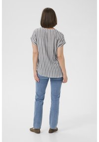 Camicia a maniche corte grigio e bianca a righe con orlo arrotondato, abbinata a jeans dritti azzurri e scarpe basse marroni.