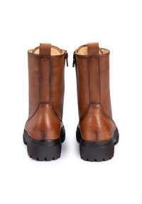 Bottines en cuir marron avec des semelles épaisses noires, des languettes à l'arrière et des zips sur les côtés, présentées de dos sur un fond blanc.