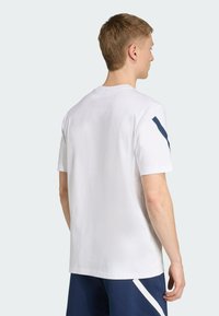 Camiseta de algodón blanca de manga corta, con un cuello redondo y un acento en azul marino en el hombro. Corte recto y textura suave.