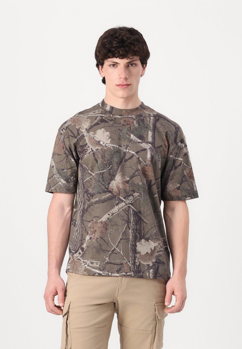 Short-sleeved camouflage t-shirt in earth tones, featuring a crew neck and a textured design with branches and leaves patterns.