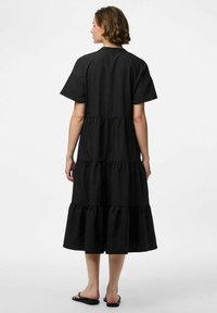 Must mustrikk kangast kleit lühikeste varrukatega, kihiline rüdisemustriga, keskpõlve pikkus, ühetooniline värv ja lihtne ümmargune kaelus. Näha on sandaale.