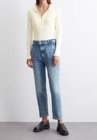 Vaaleankeltainen, ribbineuloksinen pitkähiha-paita, jossa on poolokaulus ja napit, yhdistetty haalistuneisiin sinisiin suoralahkeisiin farkkuihin ja mustiin loafer-kenkiin.