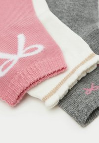 Tre paia di calze: rosa con un design bianco, bianche con un bordo oro e grigie con un logo rosa. Texture a maglia e colori vari.