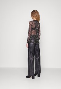 Zwarte doorzichtige top met lange mouwen en bloemmotief, met plooidetails aan de achterkant, gecombineerd met wijde zwarte leren broek en blokhak schoenen.