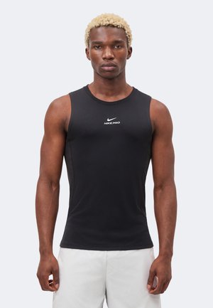 Mand med kort blondt hår iført en sort ærmeløs Nike Pro atletiktrøje og lyse shorts, står med fronten mod kameraet.