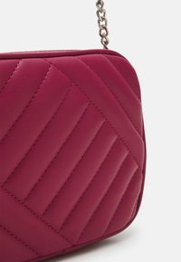 Borsa a tracolla trapuntata in pelle rosa brillante, con cuciture diagonali, una tracolla a catena e una forma rettangolare arrotondata.