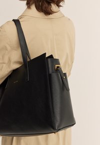 Borsa tote in pelle nera con un design strutturato, caratterizzata da un accent gold, superficie testurizzata e manici sottili.