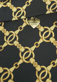 Černá tkanina s vzorem žluto-zlatého řetězu a malou srdcovou kovovou značkou s vyrytým nápisem "TWINSET MILANO".