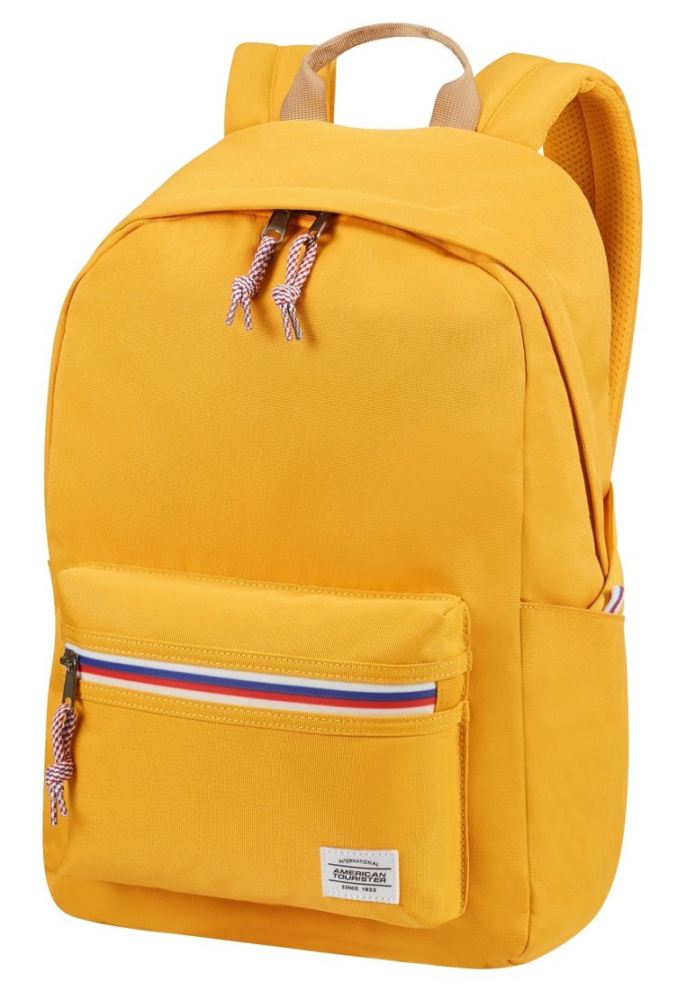 Sac à dos en tissu jaune avec des bretelles rembourrées, une poche avant zippée avec une bande tricolore, et un patch logo sur le devant.