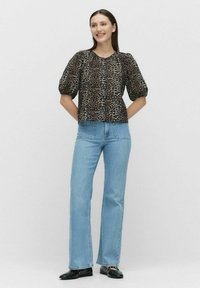 Bluse med leopardmønster og korte puffærmer, rund halsudskæring og knaplukning, parret med lyseblå flared jeans og sorte flade sko.