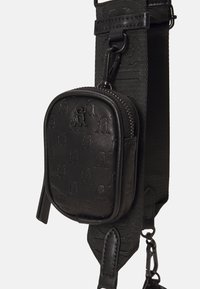 Sac en cuir noir avec motif de logo embossé. Dispose d'une fermeture éclair et d'une bandoulière détachable en tissu noir texturé. Forme carrée compacte.