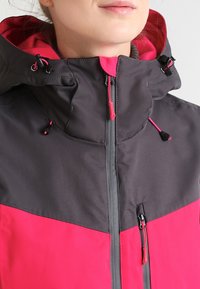 Giacca colorata con un corpo grigio e una sezione inferiore di un vivace rosa. Include una chiusura con zip, cappuccio regolabile e dettagli con cordoncino.