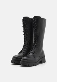Black leather knee-high boots with a chunky sole, featuring prominent eyelets, laces, and a matte finish. Side zipper for easy wear.