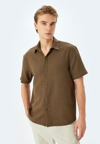 Braunes kurzärmliges Hemd mit Knöpfen, Kragen und aus strukturiertem Stoff gefertigt. Es hat fünf Knöpfe auf der Vorderseite und ein lässiges Design.