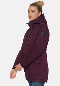 Maroon parka jacket with a hood, featuring a zip and button closure, two front pockets, and a textured patch on the sleeve.