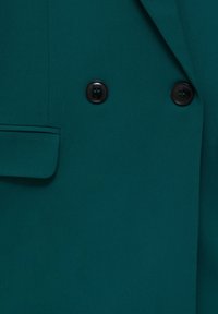 Turkusowy płaszcz dwurzędowy z zaokrąglonymi ramionami, z dwoma czarnymi guzikami i detalem bocznej kieszeni. Gładka tekstura materiału.