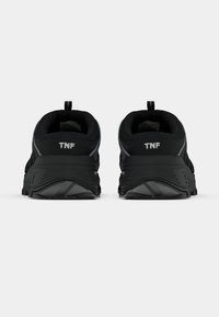 Ζευγάρι μαύρα αθλητικά παπούτσια εμφανιζόμενα από πίσω με το λογότυπο «TNF» στη φτέρνα και μαξιλαρωμένες σόλες σε απλό λευκό φόντο.