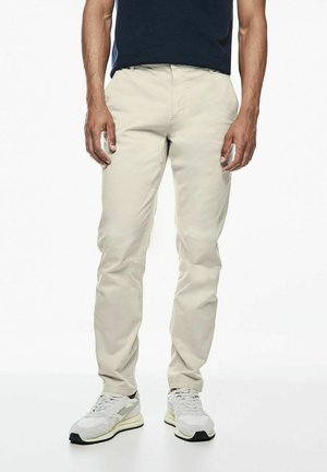 Chinos slim-fit de couleur crème avec une texture lisse, dotés d'une taille standard, de poches, et associés à des baskets grises claires.