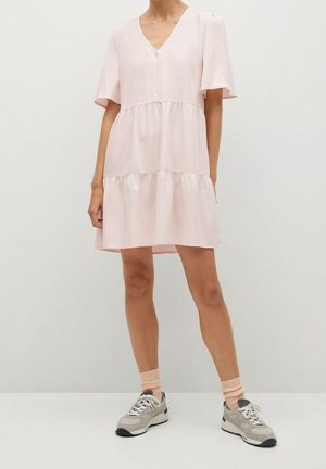 Vestito rosa chiaro a maniche corte con scollo a V, bottoni frontali e orlo a balze a più livelli. Tessuto liscio dalla morbida consistenza. Indossato con sneakers.