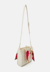 White leather handbag with quilted texture, gold hardware, and a long adjustable strap. Features red patterned silk scarf accents.