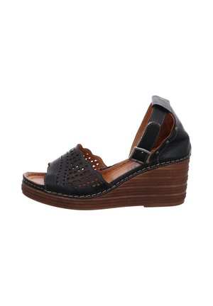 Black leather wedge sandal with perforated design and scalloped edges. Brown layered sole and adjustable ankle strap with silver hardware.