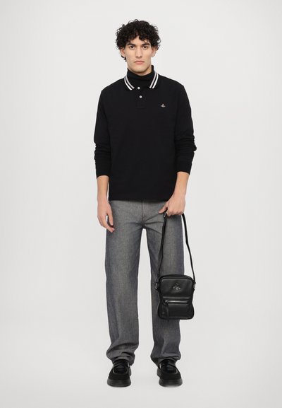 Svart långärmad polo med vita ränder, grå raka jeans, svart väska och svarta skor. Modellen poserar mot en enkel bakgrund.