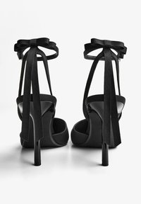 Sandali neri con tacco alto, caratterizzati da fiocchi in satin alle cinghie alla caviglia, una texture morbida e un design elegante con punta affusolata e tacco a spillo.