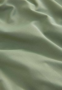 Textil mit sanften, gedämpften Grüntönen und subtilen diagonalen Rippungen, das glatte, fließende Falten und einen schimmernden Glanz zeigt.