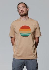 Beige t-shirt met een cirkelvormige afbeelding met horizontale strepen in rood, oranje, roomkleurig, teal en bruin. Soepele, lichtgewicht stof.