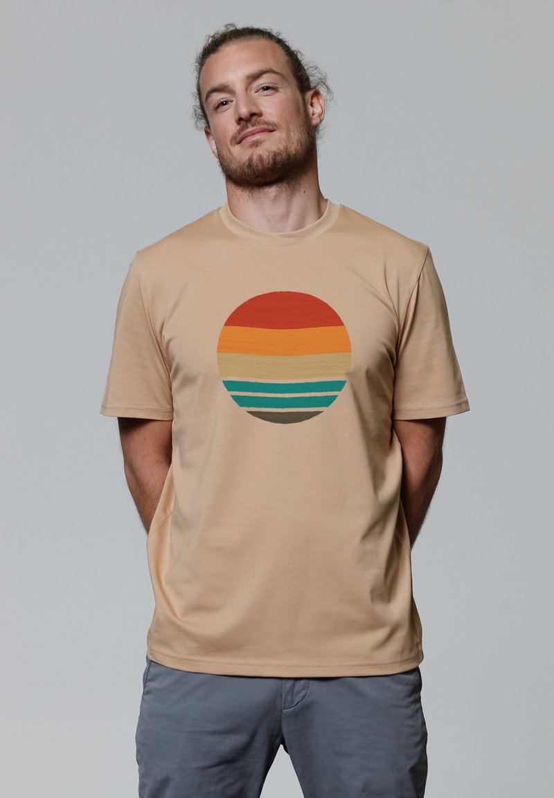 Beige t-shirt met een cirkelvormige afbeelding met horizontale strepen in rood, oranje, roomkleurig, teal en bruin. Soepele, lichtgewicht stof.