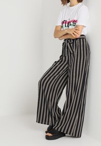 Černé a béžové pruhované široké kalhoty s papírovým pasem a zavazováním. V kombinaci s bílým tričkem s grafickým potiskem a černými platformovými sandály.